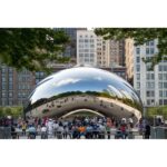 Cloud Gate sculpture in Chicago with city skyline and visitors, captured in a vibrant urban setting.
