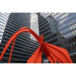 Modern sculpture in front of tall glass buildings in a cityscape.