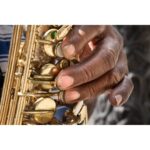 Close-up of a person's hand playing a saxophone outdoors.