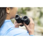Person using binoculars outdoors, focusing on nature observation.