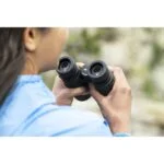 Person using binoculars outdoors, focusing on nature observation.