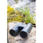 Nikon binoculars on a rock near water, ideal for outdoor photography enthusiasts.