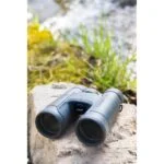 Nikon binoculars on a rock near water, ideal for outdoor photography enthusiasts.