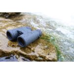Waterproof binoculars on wet rock by a stream, ideal for outdoor photography and wildlife observation.