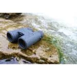 Waterproof binoculars on wet rock by a stream, ideal for outdoor photography and wildlife observation.
