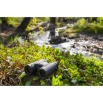 Binoculars on grass near a stream in a forest setting.