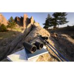 Binoculars and map on rocks with scenic view, ideal for outdoor photography gear.