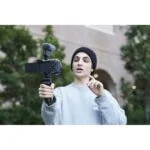 Person holding a mirrorless camera with microphone and grip, outdoors.