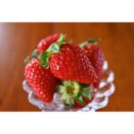 Close-up of fresh strawberries in a glass bowl on a wooden table.