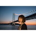 Woman standing by a lit bridge at sunset, showcasing photography capabilities.