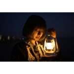 Woman holding a lantern at night, illuminating her face.