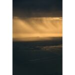 Dramatic sunset over a coastal landscape with golden light and dark clouds.
