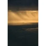 Dramatic sunset over a coastal landscape with golden light and dark clouds.
