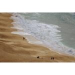 Aerial view of a sandy beach with waves and people walking along the shore.