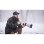 Photographer with a telephoto lens in a foggy outdoor setting.