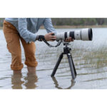 Photographer using a Sony camera with a telephoto lens on a tripod in water.