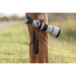 Person holding a Sony camera with a large telephoto lens outdoors.