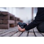 Person holding a digital camera on a wooden deck, showcasing photography gear.