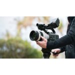 Person using a professional video camera on a tripod outdoors.
