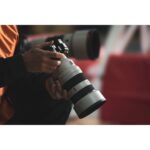 Person holding a professional camera with a large telephoto lens.