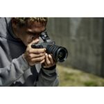 Person using a mirrorless camera outdoors, capturing a photo.