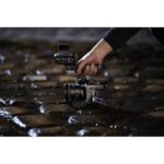 Person holding a professional video camera on wet cobblestones, showcasing photography gear.