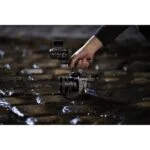 Person holding a professional video camera on wet cobblestones, showcasing photography gear.