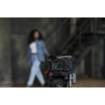 Mirrorless camera on tripod in studio setting, capturing a model in the background.