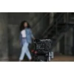 Mirrorless camera on tripod in studio setting, capturing a model in the background.