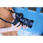 Person holding a Nikon mirrorless camera with a lens outdoors.