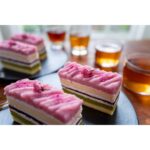 Close-up of layered cakes with pink frosting and drinks on a table.