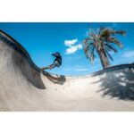 Skateboarder performing a trick in a sunny skate park, captured with professional camera gear.
