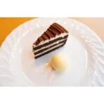 Slice of chocolate cake with cream layers and a scoop of ice cream on a white plate.