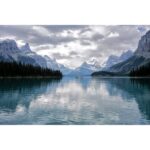Scenic view of a tranquil lake surrounded by mountains under a cloudy sky.