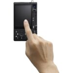 Person holding a compact digital camera, rear view showing controls and screen.