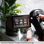 Person using a Panasonic camcorder with a digital display, near a plant.