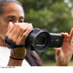 Person using Panasonic 4K camcorder outdoors, focusing on lens and grip.