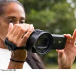 Person using Panasonic 4K camcorder outdoors, focusing on lens and grip.