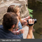 Man and child using a Panasonic LUMIX camera outdoors.