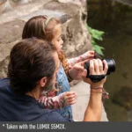 Man and child using a Panasonic LUMIX camera outdoors.