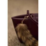 Close-up of a maroon handbag with a fur keychain, showcasing texture and detail.