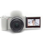 Sony mirrorless camera with flip screen displaying a smiling person, ideal for vlogging and photography.