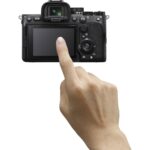 Person interacting with a mirrorless camera's touchscreen, showcasing photography gear.