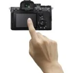 Person interacting with a mirrorless camera's touchscreen, showcasing photography gear.