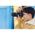 Person using a Sony mirrorless camera with a large lens outdoors.