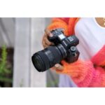 Person holding a Nikon mirrorless camera with a zoom lens outdoors.