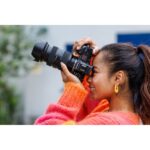 Woman using a DSLR camera with a zoom lens outdoors.