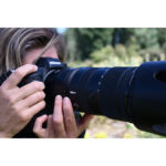 Photographer using a Nikon DSLR camera with a large telephoto lens outdoors.