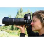 Person using a Nikon camera with a telephoto lens outdoors.