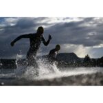 Two athletes running through water during a triathlon, captured in dynamic motion.
